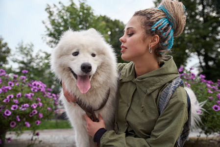 一个年轻时尚的女孩与辫子和她的白色萨摩耶狗的大详细的横向肖像。带着爱心的表情, 她抱着狗看着他
