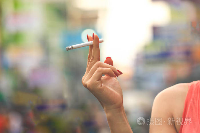 女性手拿香烟,指甲涂在五颜六色的背景上