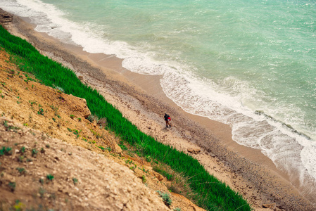 一个人沿着蓝色的海岸走在悬崖的背景下