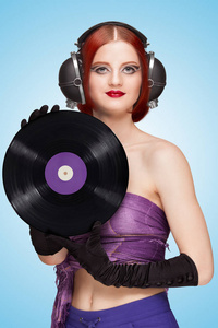 五颜六色的照片，一个美丽的女孩戴着大老式音乐耳机，手中拿着一张紫色的LP微槽乙烯基唱片在蓝色背景上。