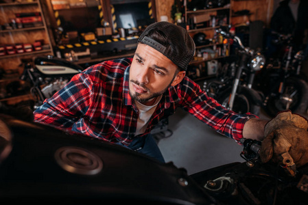 特写镜头英俊的自行车修理站工人看着车库里的摩托车