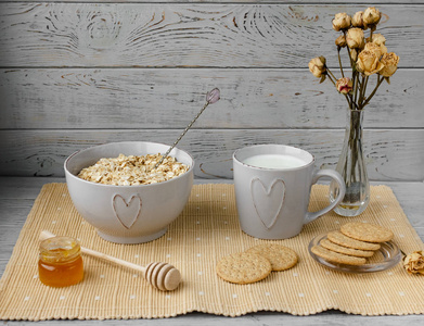 健康早餐燕麦片麦片杯牛奶罐自制果酱燕麦饼干。 背景上花瓶里的花。 碟子上的椰子饼干。 精致浪漫的早餐。 食物博客想法