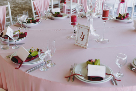 美丽的装饰婚礼宴会下的遮阳篷, 粉红色, 勃艮第和白色色调。桌子设置在大厅与板材, 餐具, 玻璃, 餐巾和卡片, 装饰的花卉组合