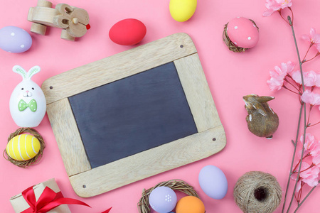 桌面上的装饰镜头，快乐复活节的背景概念。平躺在现代粉红纸上的小兔子蛋和花和兔子娃娃在空白的空间黑板模拟设计。