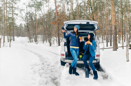 冬天森林里，两个年轻的女人坐在汽车后备箱里