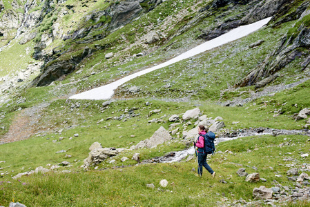 在罗马尼亚洛基山脉附近的美丽的绿色草地上漫步的女性游客。女子登山者健康生活方式壮观山景坡径路旅游惊险景观