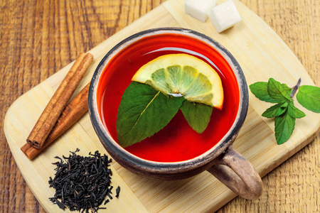 健康的热饮料在乡村粘土陶器。 黑塞隆茶，新鲜薄荷叶和柠檬放在木桌上。 上面的风景。