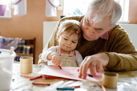 可爱的小婴儿学步的女孩和英俊的祖父在家里画的彩色铅笔。孙和人一起乐趣