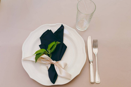 美丽而精致的婚礼庆典装饰在一个绿色的花园中间。一张餐桌上覆盖着米色桌布, 有一块盘子, 餐巾上有一根树枝, 刀叉和一只玻璃。