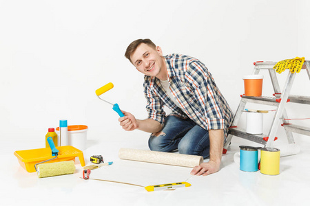 年轻人坐在地板上, 墙纸卷, 油漆辊, 装修工具, 在白色背景下隔离的公寓房间。墙纸, 胶合配件, 喷漆工具。修复主页概念