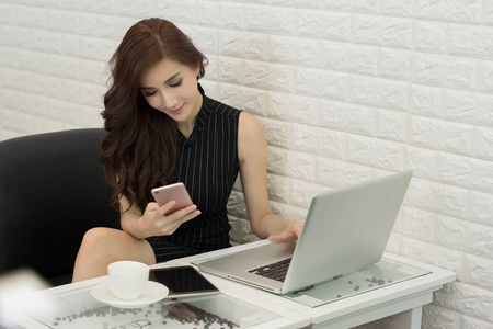 关闭年轻的商务女性使用智能手机，而她在办公室工作的笔记本电脑。