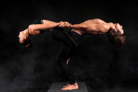Acroyoga年轻夫妇在工作室的垫子上练习瑜伽。情侣瑜伽合作伙伴瑜伽。黑白照片