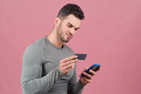 一个穿着灰色紧身 t恤衫的有魅力的男子, 拥有一款智能手机和一张银行信用卡。e 的概念