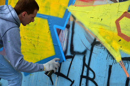 一位年轻的红头发涂鸦艺术家在墙上画了一幅新的涂鸦。 照片的过程，绘制涂鸦在墙上关闭。 街头艺术和非法破坏的概念