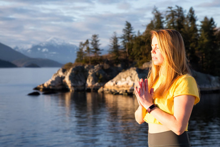 年轻女子在一个岩石岛上练习瑜伽，在一个充满活力的日落。 在加拿大不列颠哥伦比亚省温哥华西部的Whytecliff公园马蹄湾。