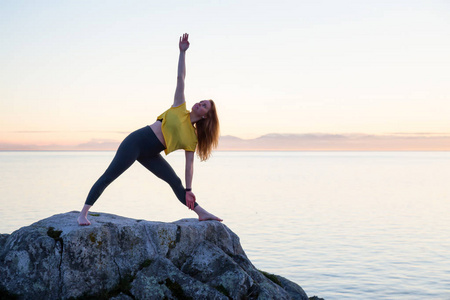 年轻女子在一个岩石岛上练习瑜伽，在一个充满活力的日落。 在加拿大不列颠哥伦比亚省温哥华西部的Whytecliff公园马蹄湾。