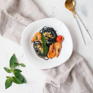 黑色意大利面，配虾西红柿和绿叶，白色盘子，配餐巾叉和勺子