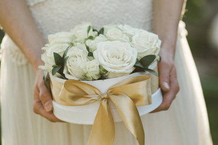 玫瑰盒。 美丽的玫瑰在白色礼品盒与金色蝴蝶结。 新娘在婚礼当天拿着花装饰。