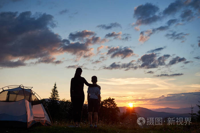 在山上一个露营的地方,站在长满野花的草地上,女人拥抱着孩子的背影