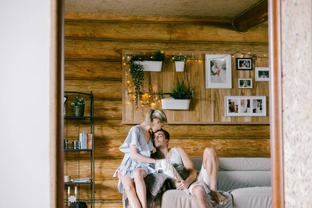 可爱的夫妇在家在一起。 漂亮的女人和迷人的男人，时髦的休闲服，坐在沙发上拥抱和亲吻。