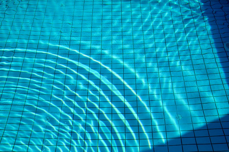 泳池底部焦线波纹和流动的波浪背景。蓝色游泳池的表面, 游泳池的水背景。清澈的浅蓝色水池水波纹与太阳反射