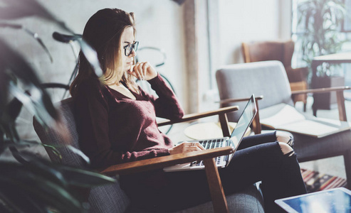 有魅力的年轻女商人穿着休闲服装, 在 coworking 办公室工作。女性使用现代移动笔记本电脑, 而坐在舒适扶手椅