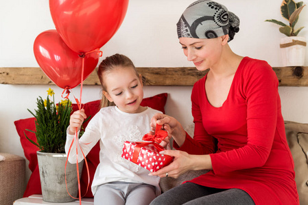 年轻的母亲癌症病人和她可爱的女儿庆祝从医院回家。 欢迎带气球和礼物的家庭或生日聚会。