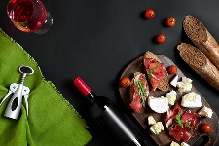 美味的开胃酒火腿, 芝士, 长方形切片, 西红柿, 在木板上服务, 在黑色表面有红葡萄酒的玻璃