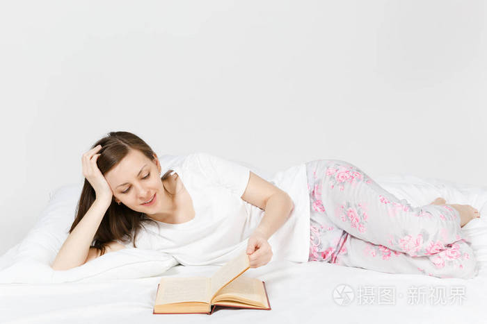 年轻快乐的女人躺在床上, 白色的床单, 枕头, 毯子在白色的背景.