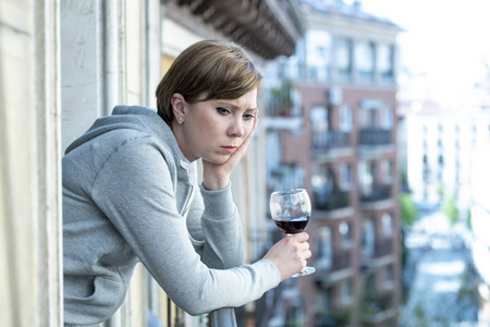 美丽的红头发的白种人妇女患有抑郁症，在家里的阳台上拿着一杯酒。 凝视着外面，感到悲伤的痛苦和悲伤。 危机抑郁与心理健康概念