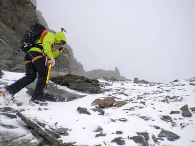 在瑞士阿尔卑斯山的恶劣天气中，雄性登山者爬上陡峭的雪和岩石坡