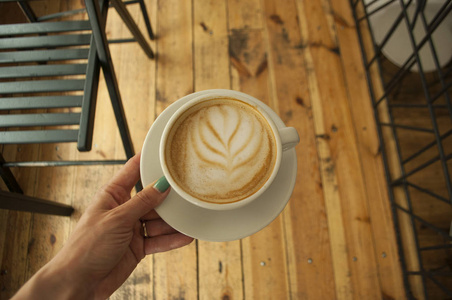 s hand with beautiful manicure holding a cup of cappuccino with 