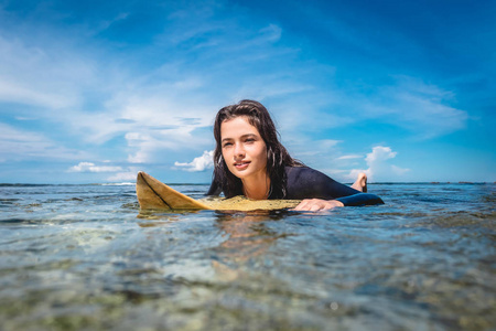 印尼巴厘岛努沙杜阿海滩冲浪板上穿湿衣的年轻女运动员肖像。