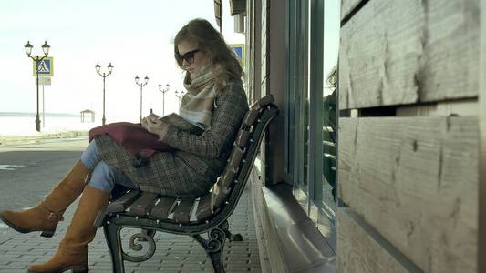 年轻, 美丽, 可爱的女人坐在公园的长凳上, 在她的笔记本手。她穿着一件大衣。她做笔记, 看起来很浪漫