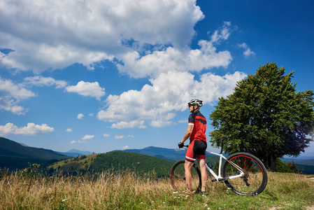 运动运动员站在草地上，骑着越野自行车，在夏日欣赏美丽的喀尔巴阡山美景，健康的生活方式和户外运动理念