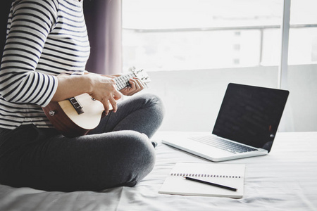 年轻的幸福女人在卧室里享受用吉他或四弦琴演奏音乐的假期放松和娱乐概念。