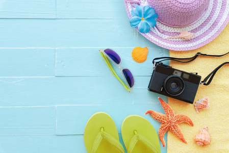 海滩配件，包括太阳镜，海星，帽子，海滩，复古相机，黄毛巾，彩色翻盖，贝壳，明亮的蓝色粉饰木背景，为暑假和假期的概念。