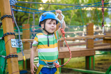 一个小可爱的男孩在夏天阳光明媚的日子里在攀岩冒险公园里享受活动。蹒跚学步的孩子在绳索操场结构中攀爬。安全攀登极限运动与头盔和卡宾