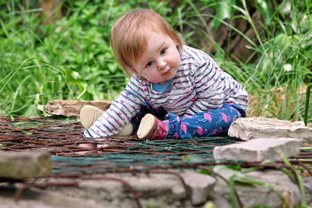 美丽的婴儿坐着微笑和摆姿势的肖像。 小可爱的女孩在花园里玩。 孩子们正在公园外面玩耍，周围是美丽的绿色树木和灌木丛的自然环境。