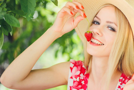 年轻的金发女人在花园里吃草莓，微笑，夏天阳光明媚，温暖的夏天，形象，自我照顾和健康的生活方式。