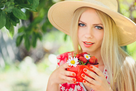 年轻的金发女人，在绿色花园的碗里放着草莓，一个夏天阳光明媚的日子，温暖的夏天，充满了形象自我关怀和健康的生活方式。