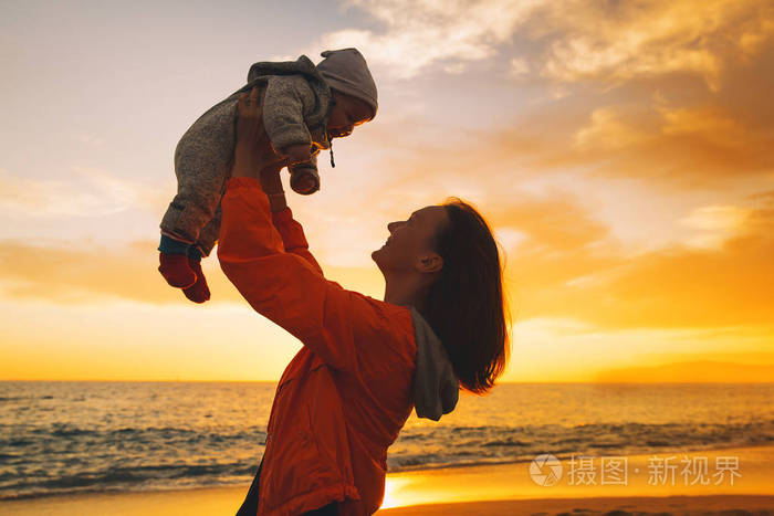 女人和她的孩子一起在海边户外玩耍 年轻的母亲在天空中抛出婴儿.
