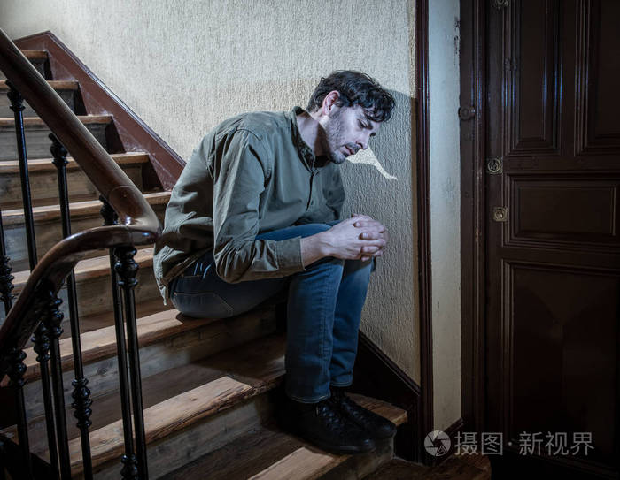 沮丧的拉丁男人坐在楼梯井里,双手抱头,感到孤独和悲伤,并在心理健康