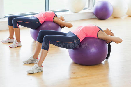 两个健康的女人在健身房的健身球上伸展