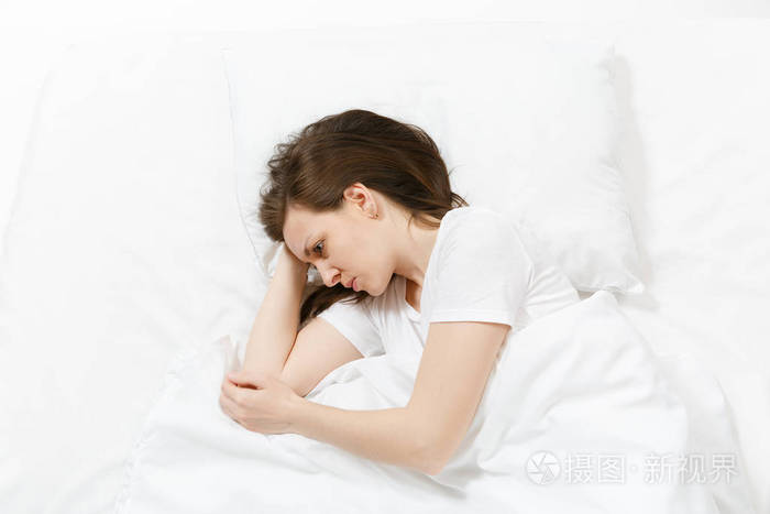 疲惫的压力,哭泣的年轻黑发女人躺在床上,用白色床单枕头毯.