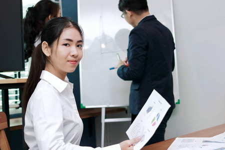 领导商业女性的概念。 自信的亚洲年轻女商人在现代办公室背景下听演讲之间微笑。