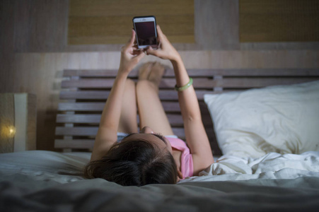 年轻漂亮快乐的女孩躺在床上，微笑着在互联网社交媒体应用程序上调情，使用手机，在卧室里欢快放松，在线约会和手机技术