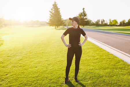 年轻的运动女孩穿着黑色制服帽，做运动锻炼，热身伸展，然后在阳光明媚的夏日在高尔夫球场公园户外的绿色草坪上跑步。 健康的生活方式