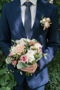 s hands. Groom in suit with wedding bouquet outdoors