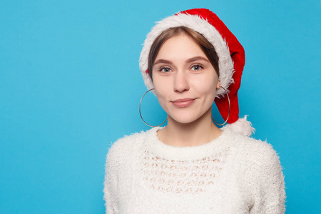 冬季圣诞节人们美容观念漂亮的金发碧眼，戴着浅蓝色背景的圣诞帽。 年轻美丽可爱开朗的女孩的肖像，微笑着看着白色背景上的相机。